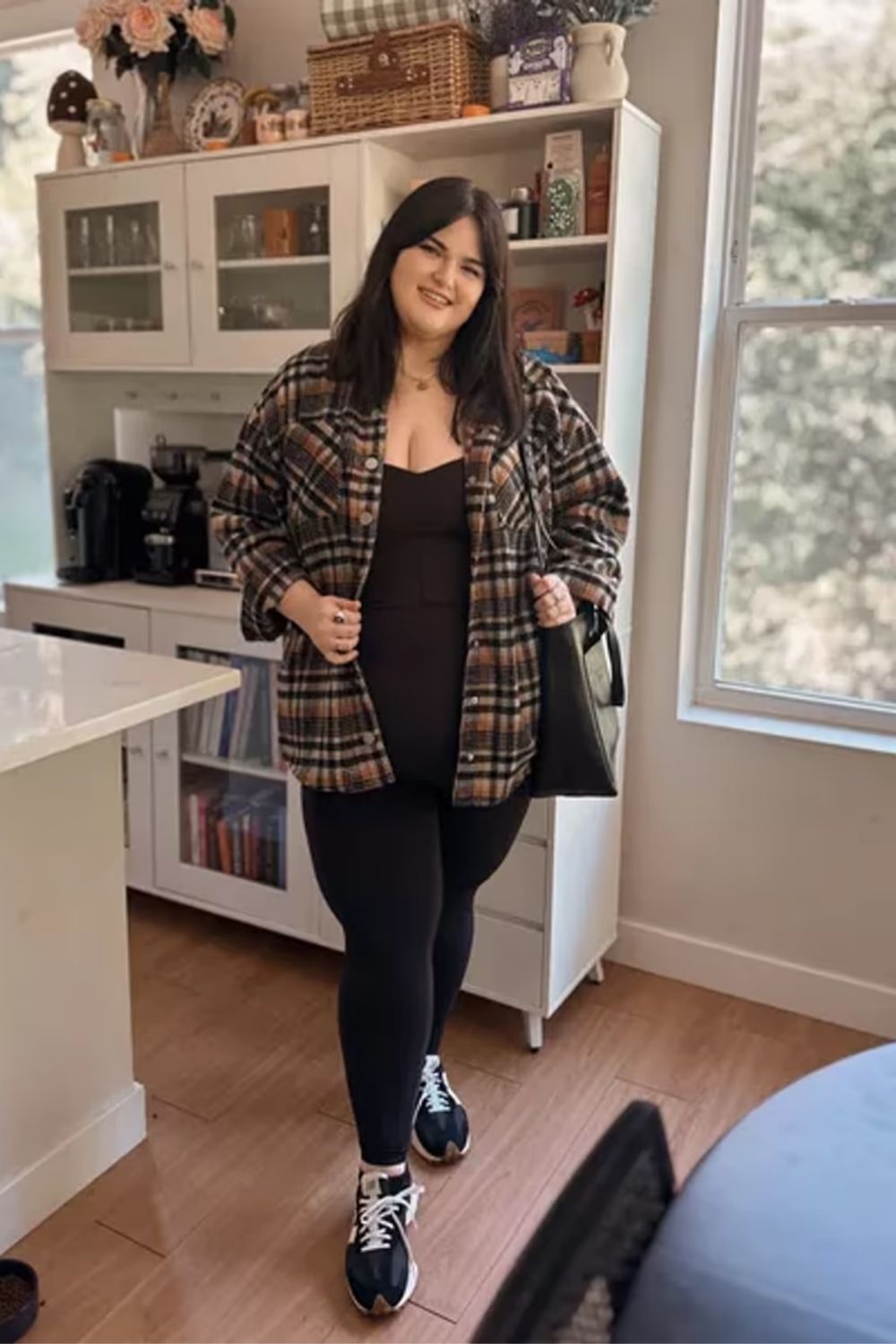 The ensemble effortlessly blends an oversized plaid shirt with chic black layers, complemented by the contrast of tight leggings and structured shoes for a stylish and comfortable look.