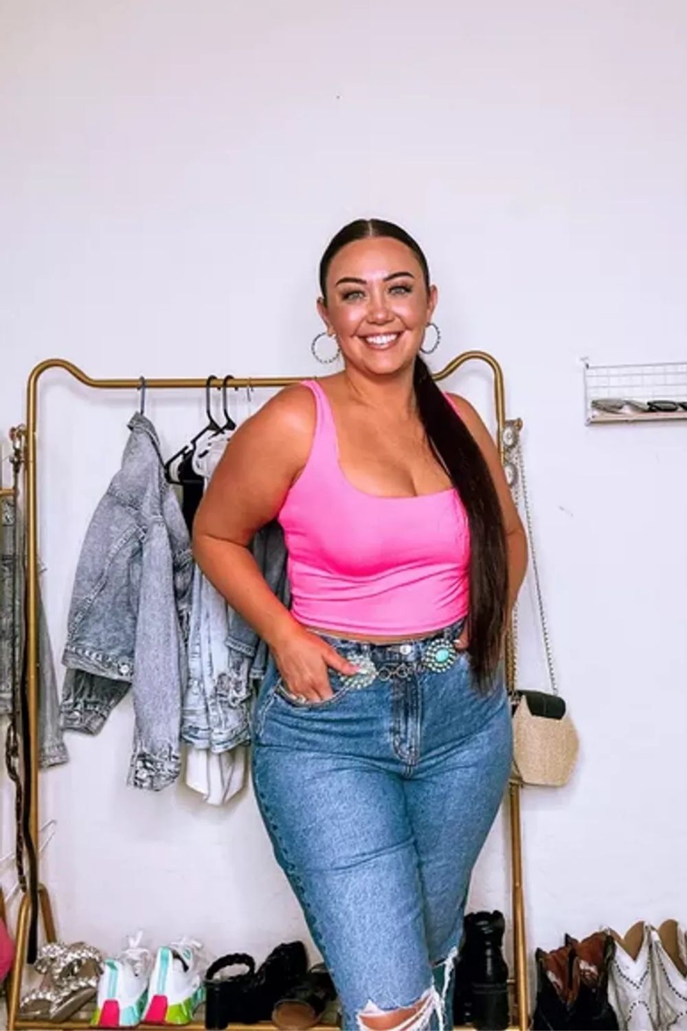 Bright pink top, high-waisted jeans, statement belt add vibrant flair.