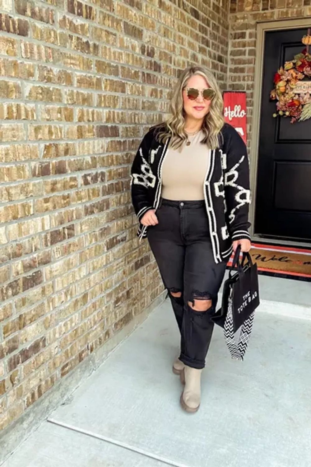This ensemble radiates chic and effortless style with a bold black and white patterned cardigan against neutral tones, complemented by distressed black jeans and beige ankle boots, harmonizing casual with sophisticated elements.