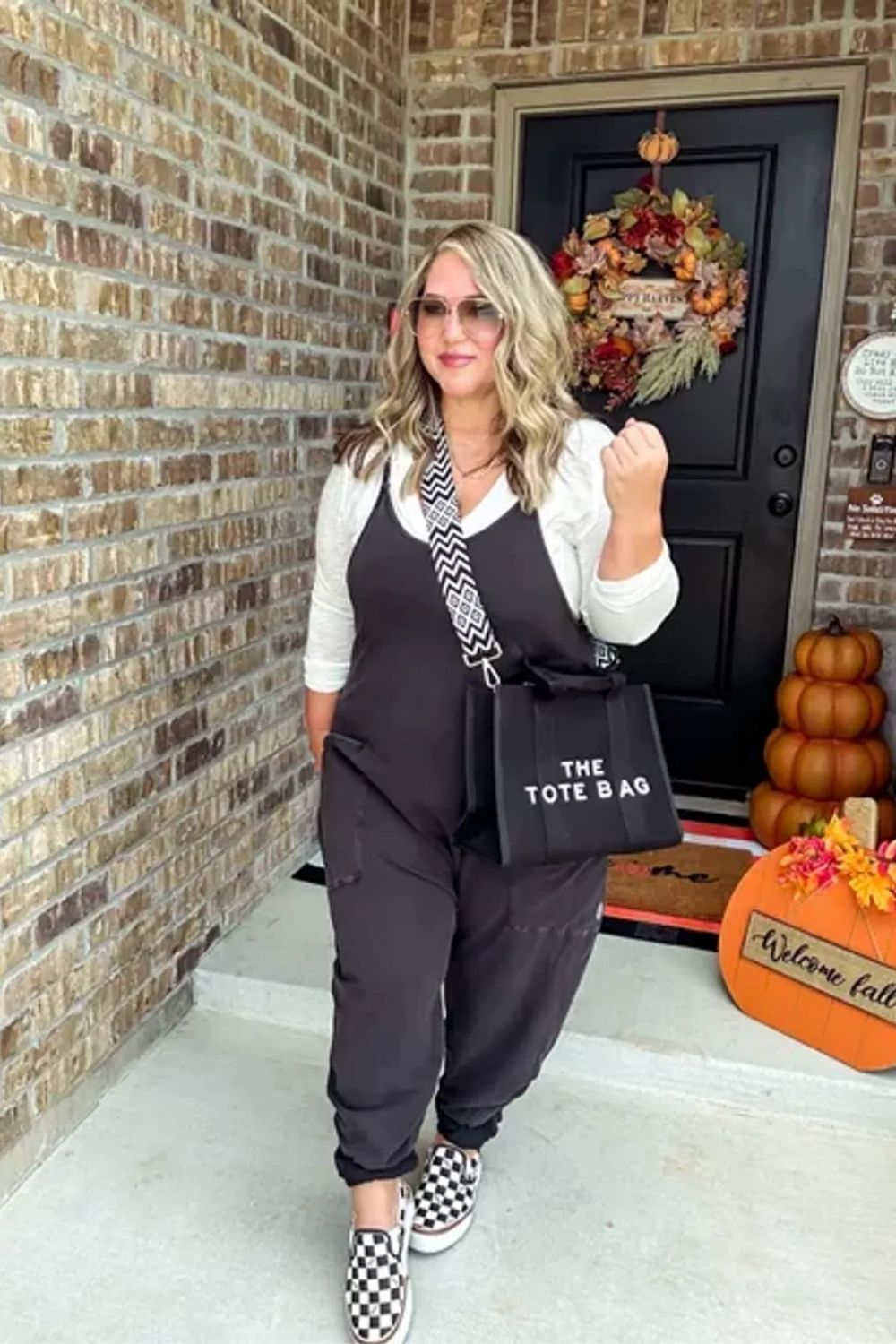Featuring a chic monochrome palette, this outfit combines a relaxed-fit jumpsuit with a crisp white blouse, accessorized with on-trend checkered slip-on shoes and a statement tote for a perfect blend of comfort and contemporary fashion.