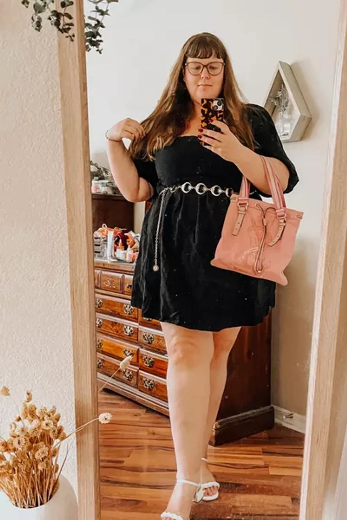 Off-the-shoulder black dress, cinched waist, pink handbag, white sandals.