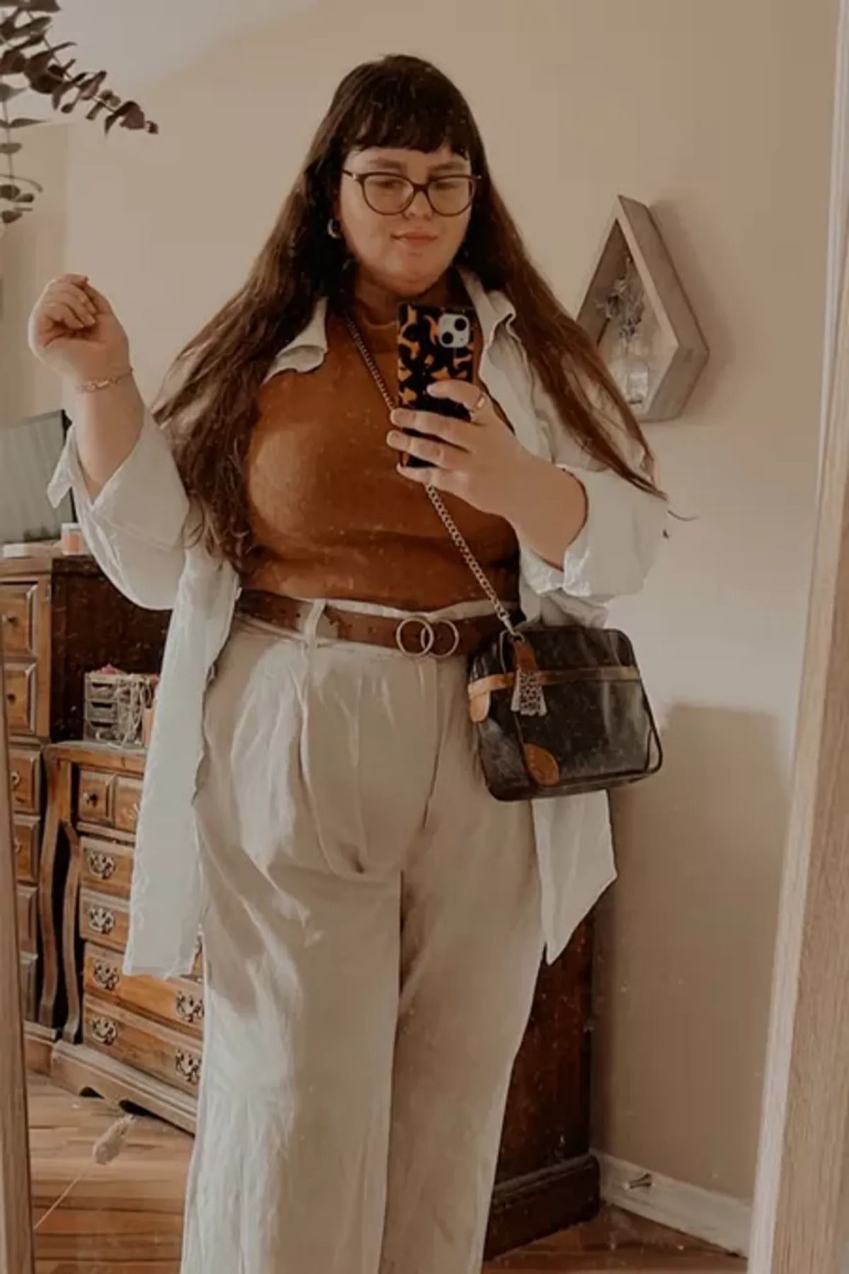 Layering with warm-toned top, crisp white overshirt, high-waisted trousers, belt.