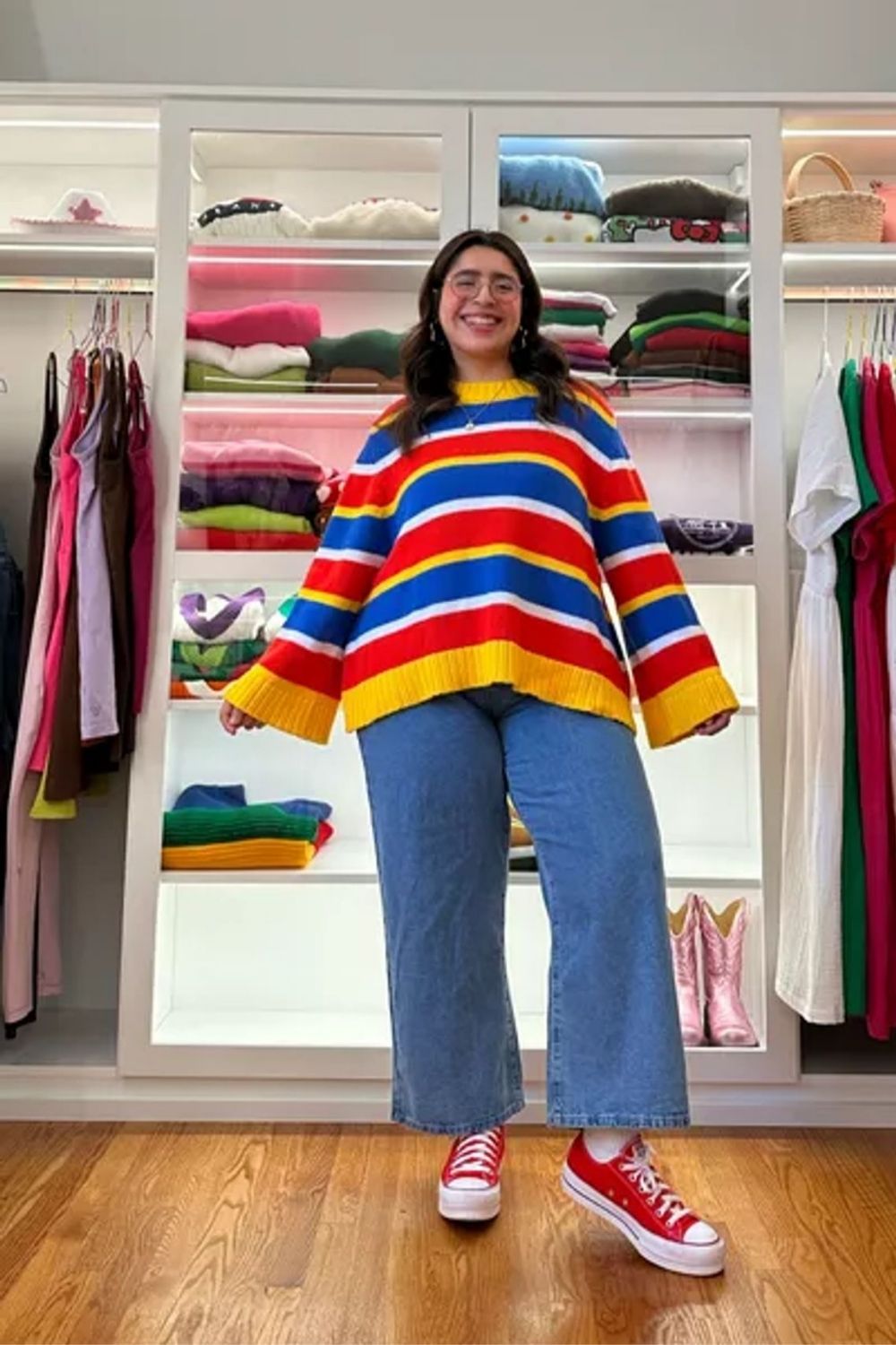 Showcasing a vibrant and playful use of color with a striped, oversized sweater, this ensemble pairs wide-leg jeans for a modern and relaxed silhouette, and classic red sneakers offer a pop of coordinating color and a casual finish to the look.
