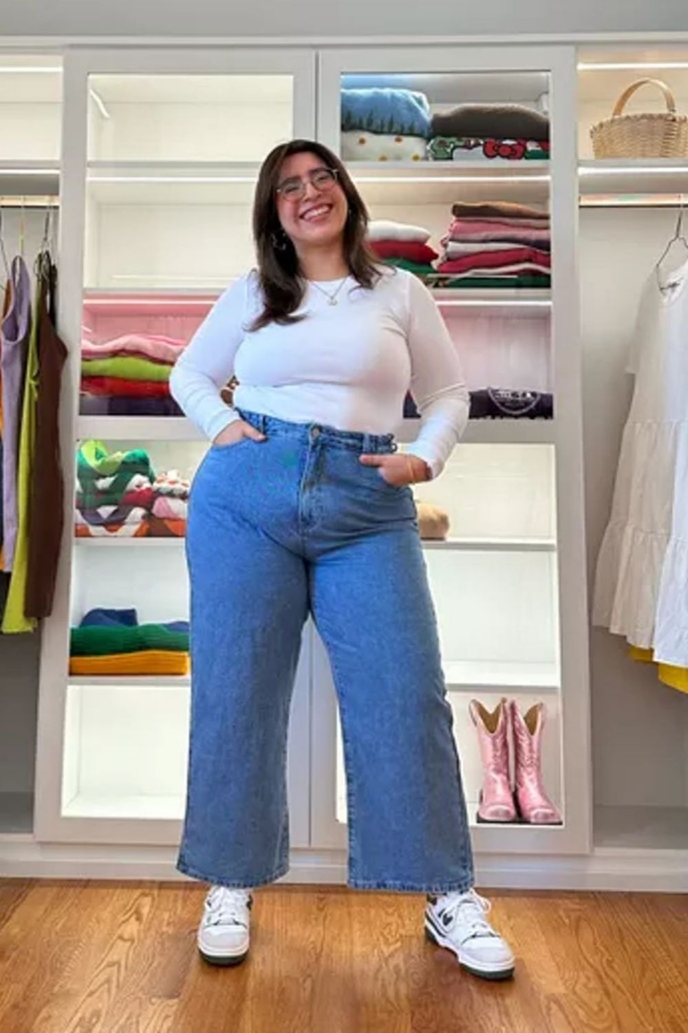 Featuring classic high-waisted wide-leg jeans, creating a flattering silhouette by elongating the legs, paired with a fitted white top that balances proportions nicely. Clean white sneakers add a casual, contemporary finish to the ensemble.