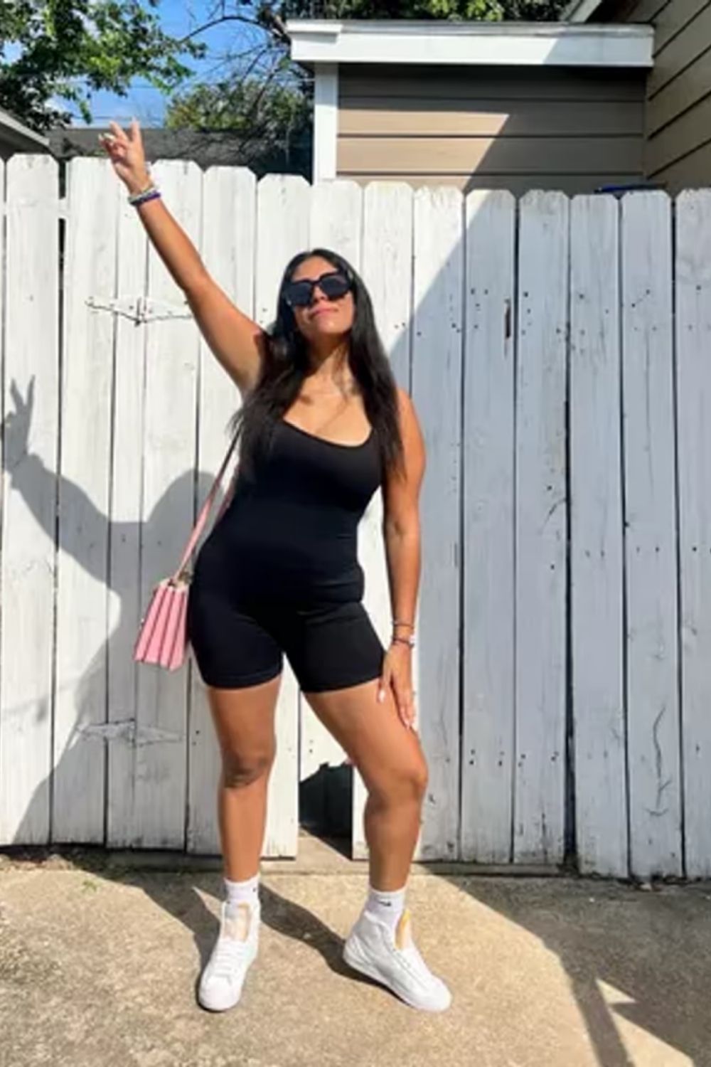Black one-piece, white sneakers, pink bag for a sleek, sporty style.