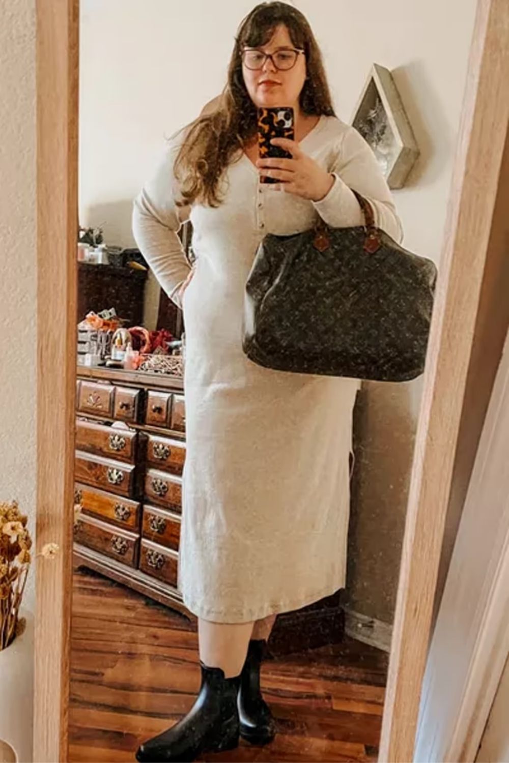A casual yet sophisticated aesthetic is embodied by a form-flattering midi dress paired with chunky black boots, complemented by a practical large tote and a neutral color palette.