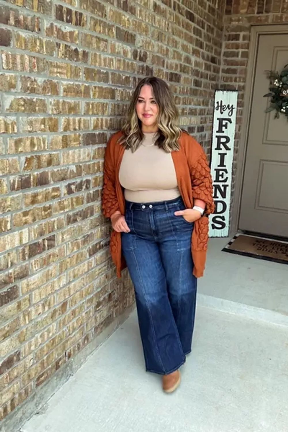 Featuring a balanced color palette with earthy tones, this ensemble pairs flared jeans and a fitted top, highlighting the silhouette, while a chunky cardigan adds a cozy, textured layer that is both stylish and practical.